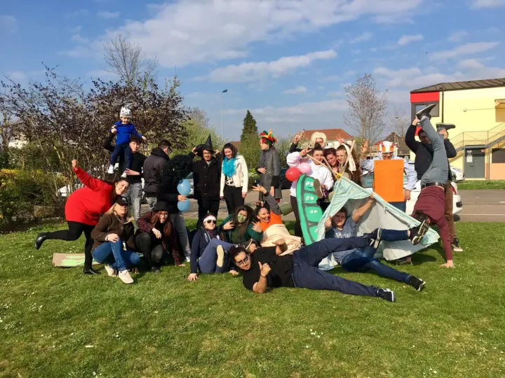 Groupe de jeunes en costumes et déguisements, certains sur une tente, sur l'herbe par beau temps.