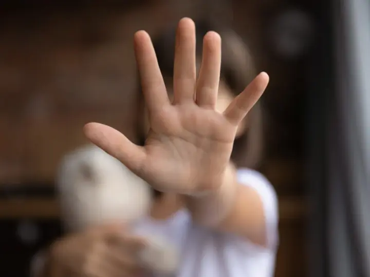 Main d'enfant tendue, stop. Un doudou flou à côté. Une image qui évoque une cellule enfance en danger.