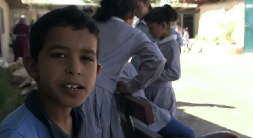 Un garçon souriant pose devant des filles en uniforme dans la même cour d'école.