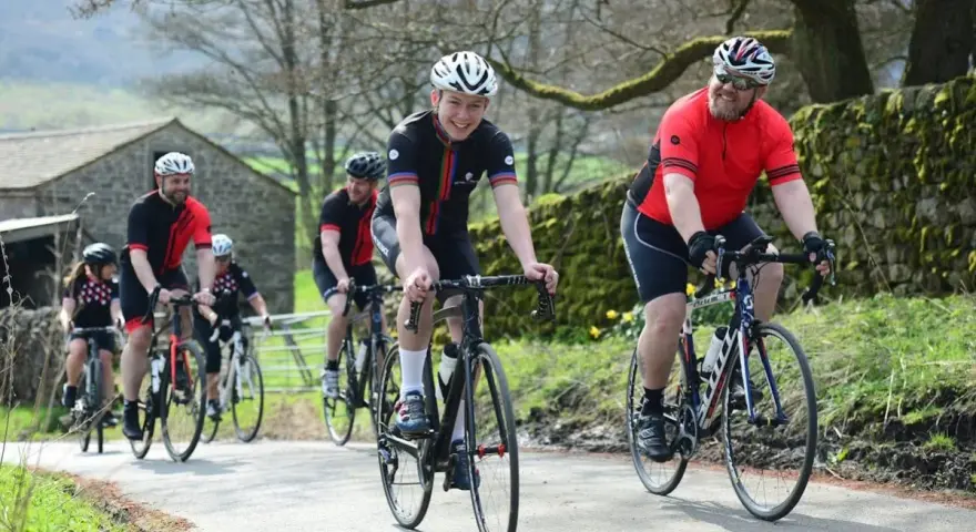 Un groupe de cyclistes souriants roule sur une route de campagne, respectant le code de la route pour cycliste en groupe.