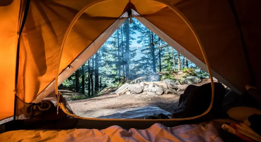 Vue de l'intérieur d'une tente orange, un feu crépite dehors. L'obligation sécurité camping est respectée avec ce campement bien installé.