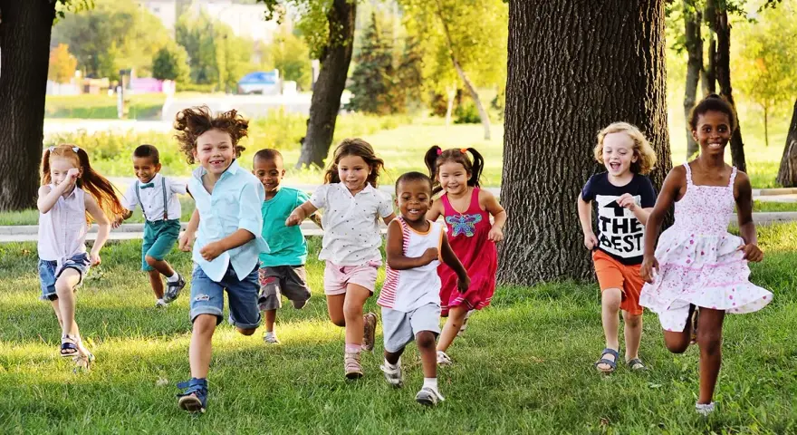 Des enfants joyeux courent dans l'herbe, profitant d'une journée ensoleillée dans une colonie de vacances 3-6 ans.