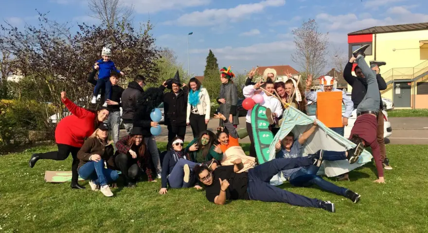 Groupe de jeunes en costumes et déguisements, certains sur une tente, sur l'herbe par beau temps.