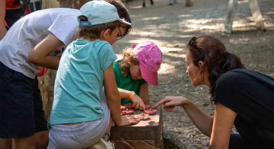 Une famille résout une énigme pour course d'orientation, manipulant des jetons sur un jeu en bois.