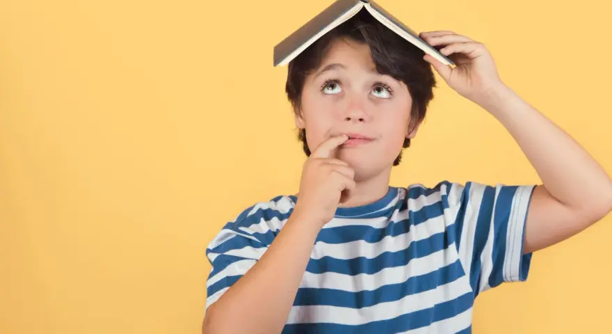 Un enfant de 5 ans, avec un livre sur la tête, réfléchit. Il est en colonie de vacances.