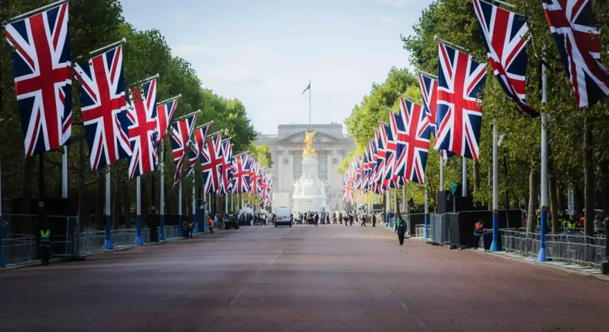 Allée bordée de drapeaux britanniques menant à un palais, avec des arbres et des gardes.
