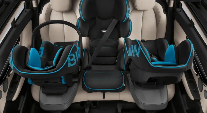 Trois sièges auto pour enfant, noir et bleu, installés sur des sièges en cuir clair. Le transport enfant en voiture est sécurisé.