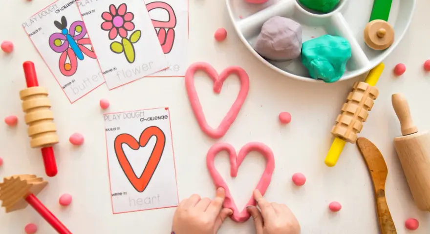 Pâte à modeler rose en forme de cœur, cartes d'activités, rouleaux et petites boules de pâte.