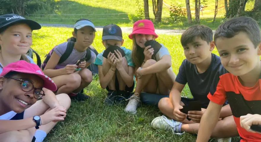 Groupe d'enfants souriants assis dans l'herbe, certains tenant des cartes.