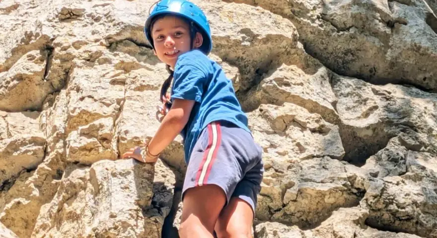 Enfant souriant escaladant un rocher avec un casque bleu.