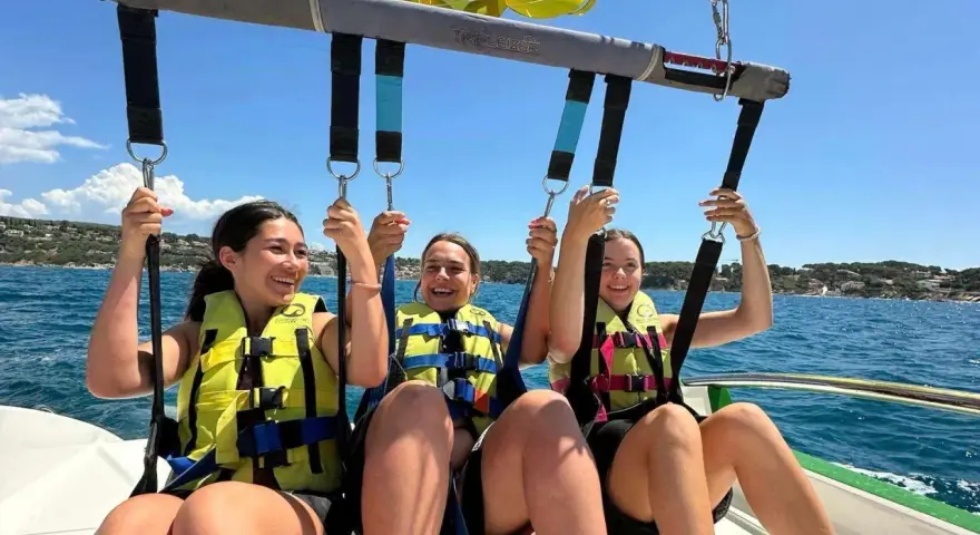 Trois jeunes femmes souriantes en parachute ascensionnel au-dessus de la mer.