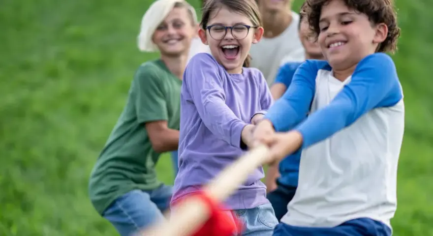 Des enfants joyeux jouent à la corde dans un champ d'herbe verte.