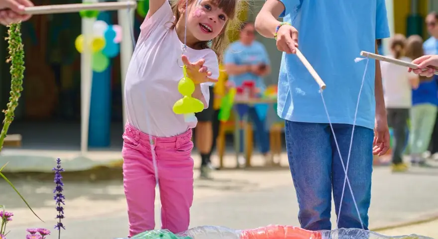 Une petite fille joyeuse participe à des jeux de kermesse pour tout petit, essayant d'attraper un jouet jaune avec une canne à pêche improvisée.