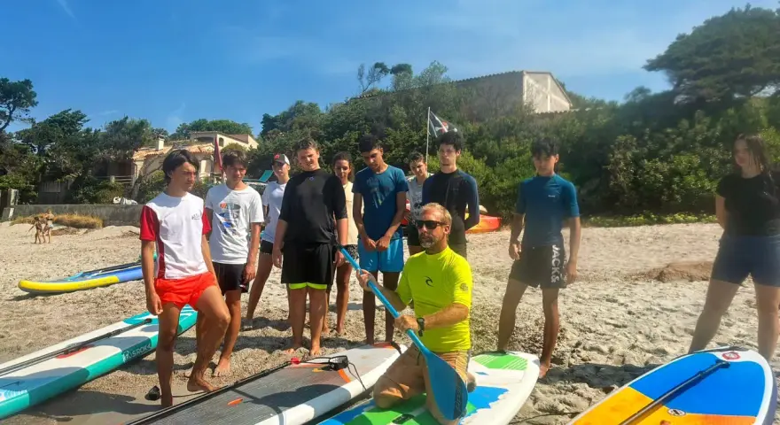 Un groupe d'adolescents et un moniteur sur une plage avec des planches de paddle.