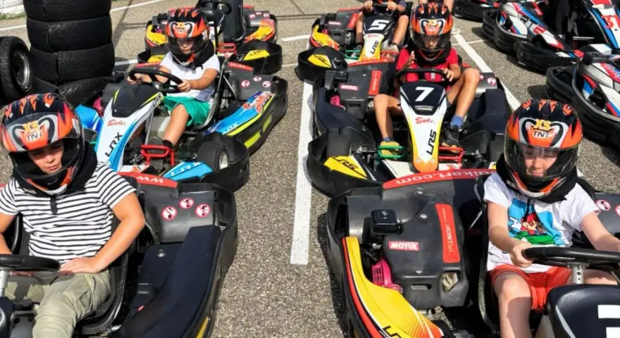 Des enfants casqués prêts pour une course de colo karting, le sourire aux lèvres, impatients de démarrer.