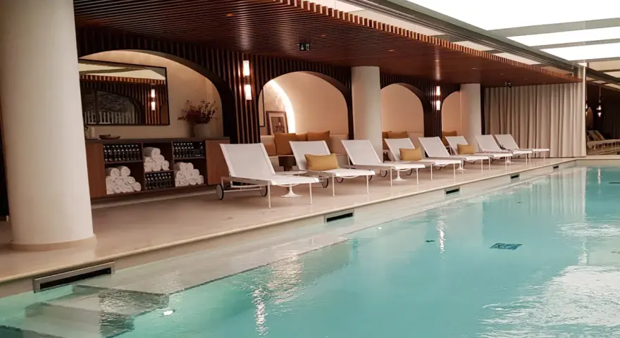Piscine intérieure avec chaises longues blanches, coussins jaunes et étagères de serviettes.