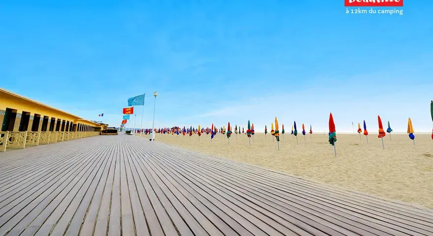 Plage de Deauville, parfaite pour une vacance scolaire en Normandie. Cabines colorées, parasols et ciel bleu azur.