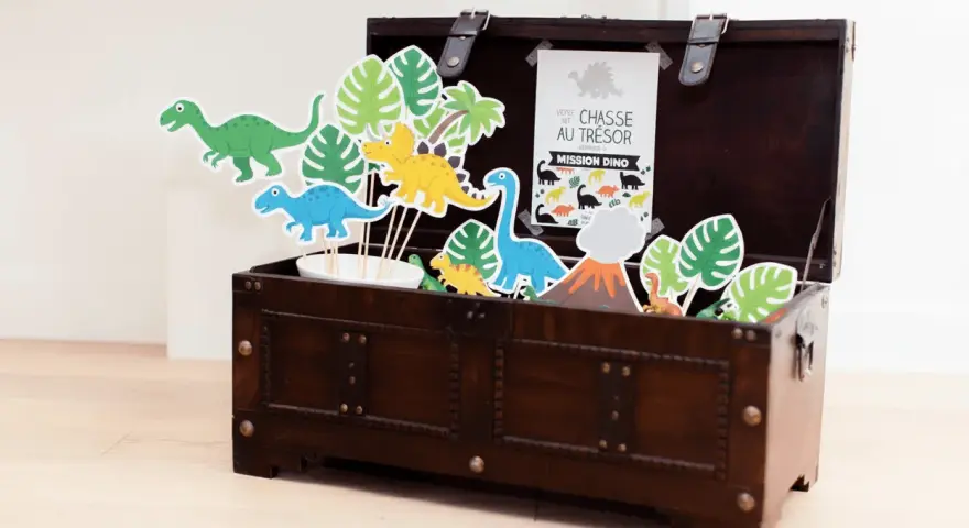 Coffre en bois rempli de décorations de dinosaures et de feuilles tropicales.