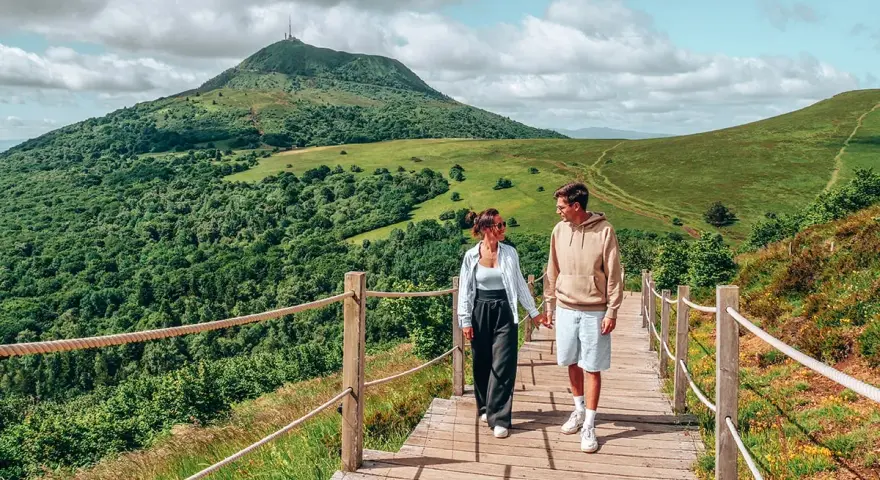 Couple marchant sur un chemin en bois avec un volcan en arrière-plan en Auvergne.