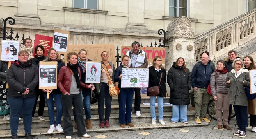 Un groupe de personnes manifeste devant un bâtiment, tenant des pancartes "Le Ministère de l'injustice".