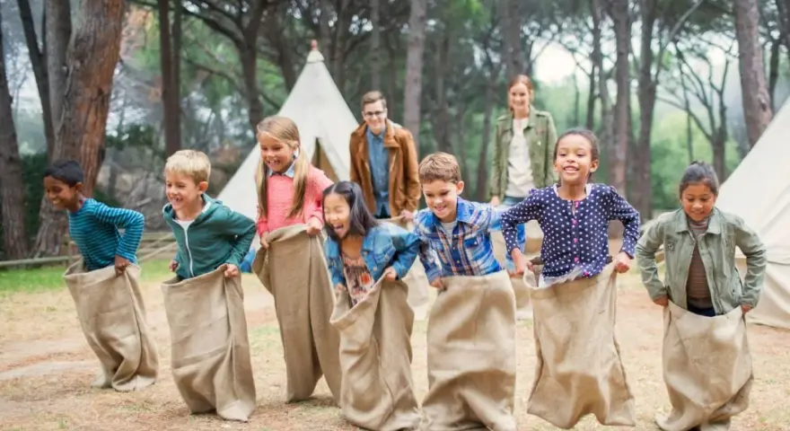 Des enfants participent à une course en sac dans un camp de vacances en forêt.