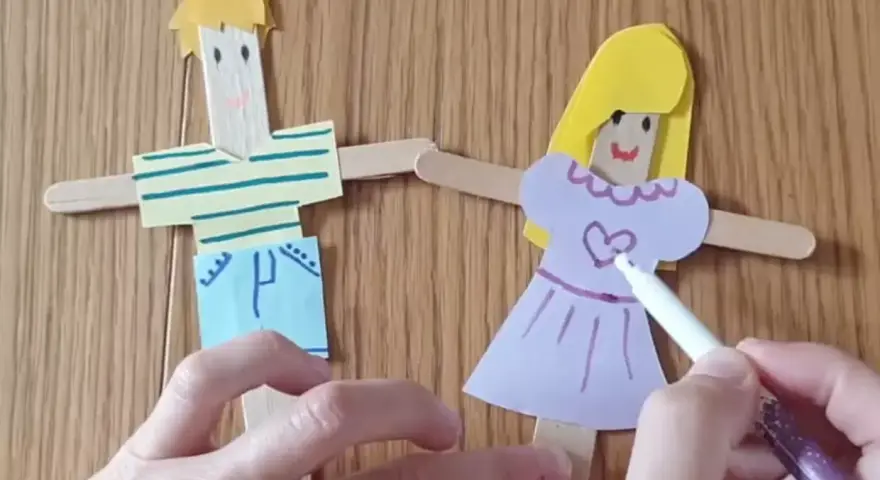 Poupées en bâtonnets de bois, une fille et un garçon, décorées par des mains d'enfant.