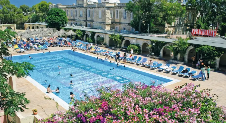 Profitez de vos vacances scolaires à Malte au bord de cette piscine animée, entourée de transats et de végétation luxuriante.