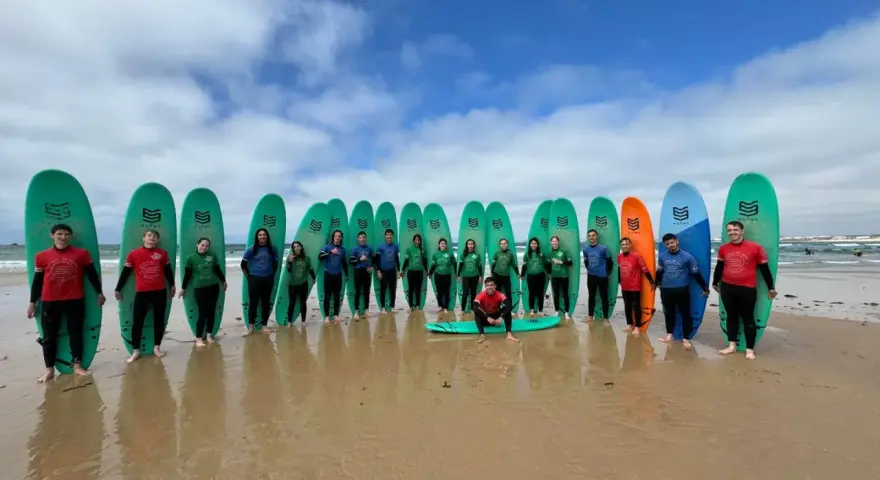 Groupe de jeunes souriants avec des planches de surf sur une plage.