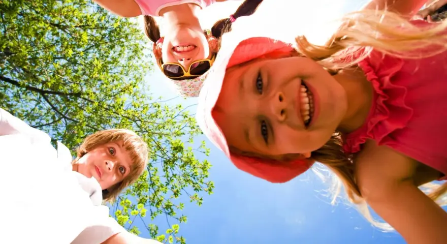 Trois enfants souriants, vus d'en bas, profitent d'une journée ensoleillée lors d'un camp sportif.