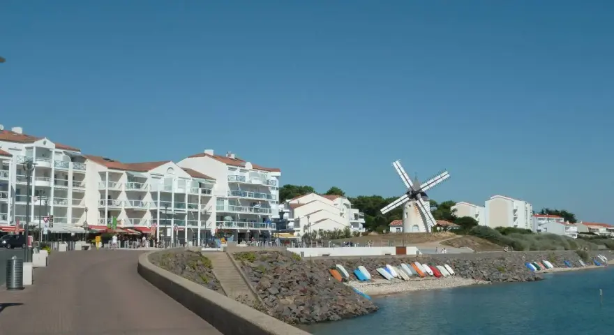 Vue de Jard-sur-Mer avec son port, ses immeubles blancs, son moulin et sa plage bordée de bateaux.