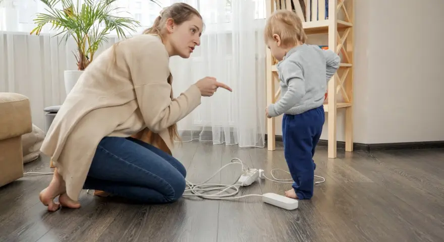 Une femme réprimande un enfant près de prises électriques au sol.