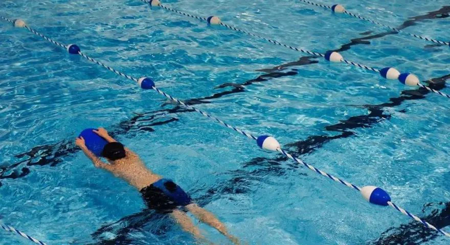 Un nageur utilise une planche bleue dans une piscine avec des lignes de bouées bleues et blanches.