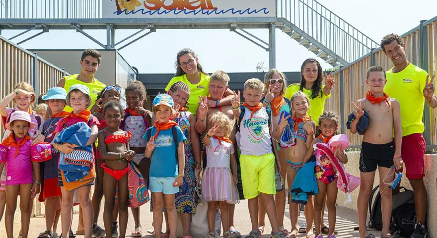 Un groupe d'enfants joyeux, portant des foulards orange, pose pour une photo de famille lors de leurs vacances.