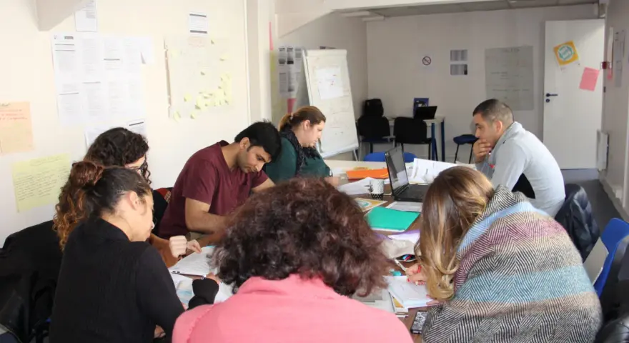 Groupe de personnes assises autour d'une table, travaillant sur des documents et un ordinateur portable.