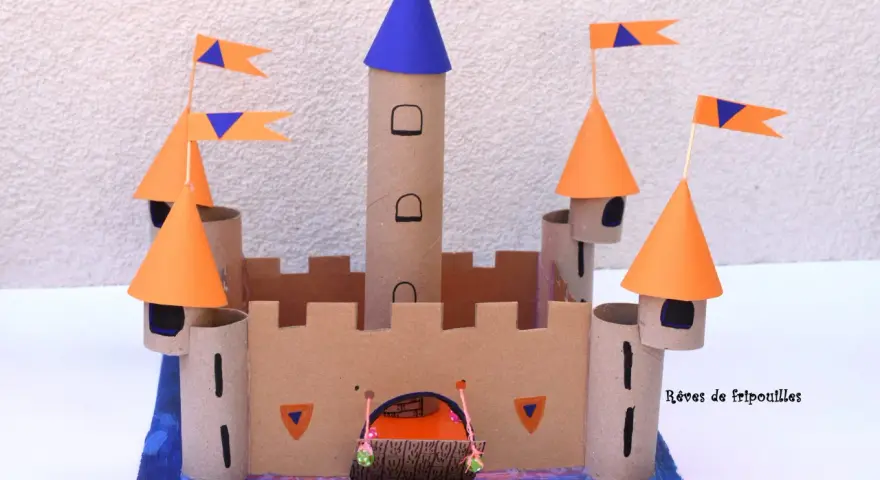 Château fort en carton avec tours, drapeaux orange et bleus, et une herse.