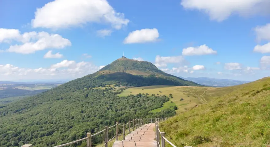 Escalier en bois menant au Puy de Dôme sous un ciel bleu et nuageux.