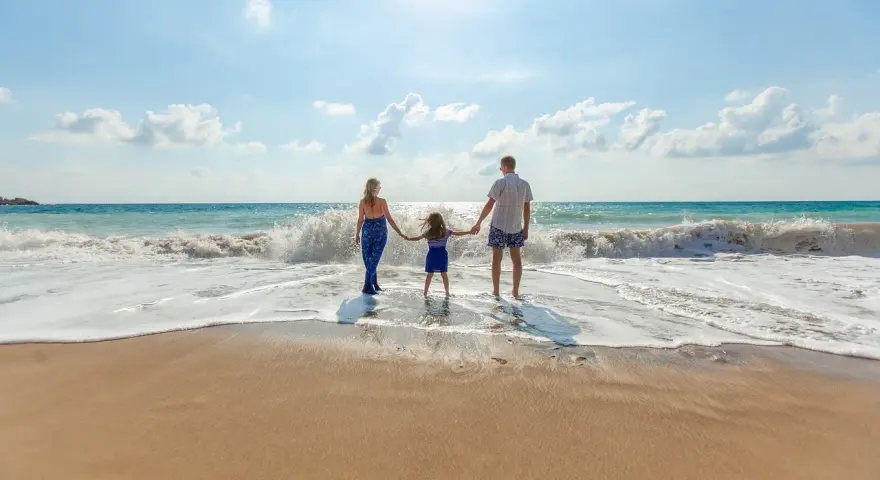 Une famille se tient la main sur la plage, profitant des vagues. Ils pensent à devenir famille d'accueil pour les vacances, offrant ces moments de bonheur.