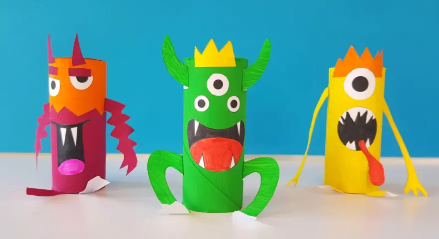 Trois monstres colorés faits à la main, en rouleaux de papier toilette, sur fond bleu.