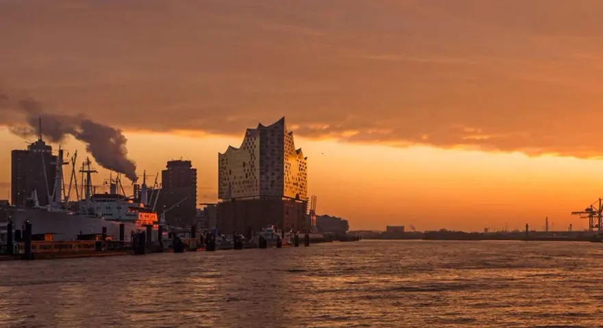 Coucher de soleil sur le port de Hambourg, idéal pour visiter Hambourg en 3 jours. Bateaux, grues et la Philharmonie de l'Elbe se reflètent sur l'eau.