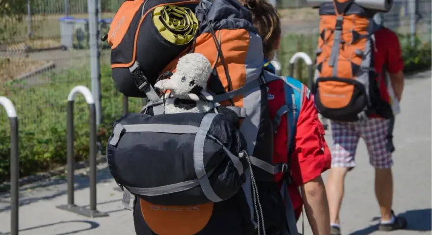 Deux jeunes partent en camp de scout, chargés de leurs sacs à dos. Un doudou mouton est accroché au sac de devant.