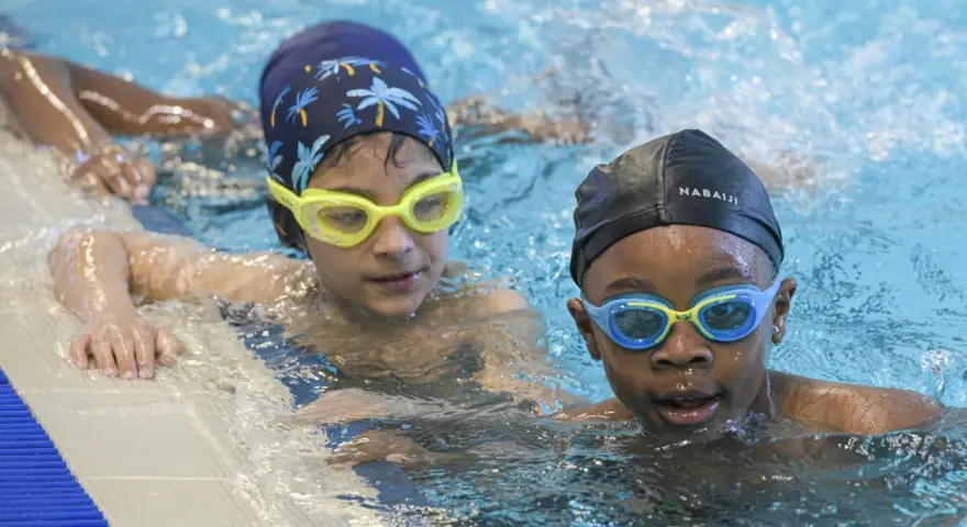 Deux enfants avec des bonnets et lunettes de natation dans une piscine.