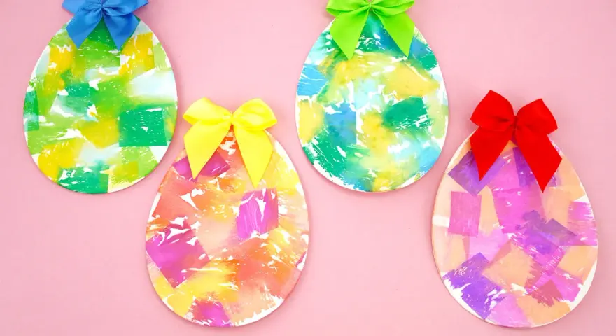 Quatre œufs décorés de papier crépon coloré et ornés de rubans sur fond rose.