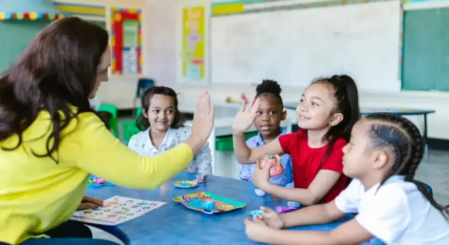 Une enseignante donne une tape dans la main à des enfants autour d'une table dans une salle de classe.