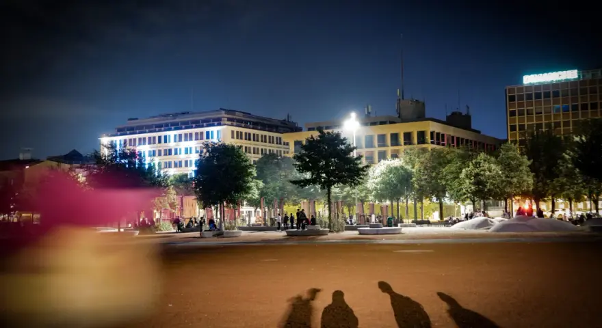 Ombre d'un mineur dehors la nuit, projetées sur une place éclairée par des bâtiments modernes.