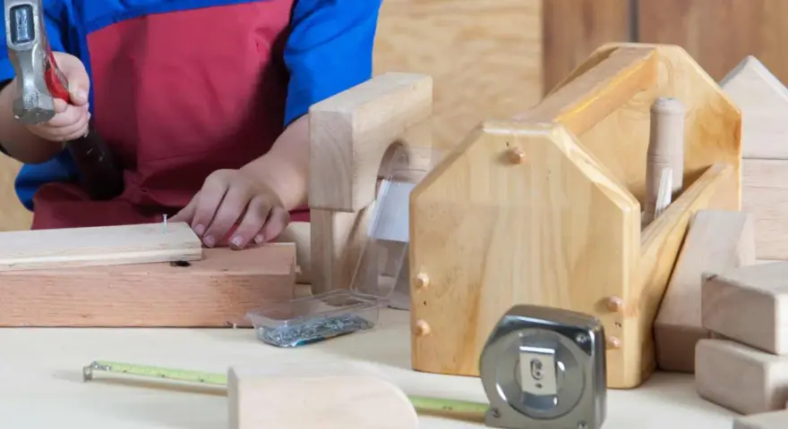 Enfant bricolant avec un marteau, des clous, un mètre ruban et des outils en bois.