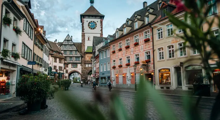Vue d'une rue pavée à Fribourg-en-Brisgau avec une tour à horloge et des bâtiments colorés.