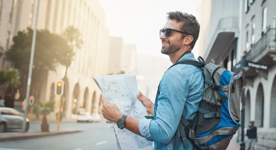 Un homme souriant avec un sac à dos consulte une carte, prêt pour un voyage en immersion dans la ville.