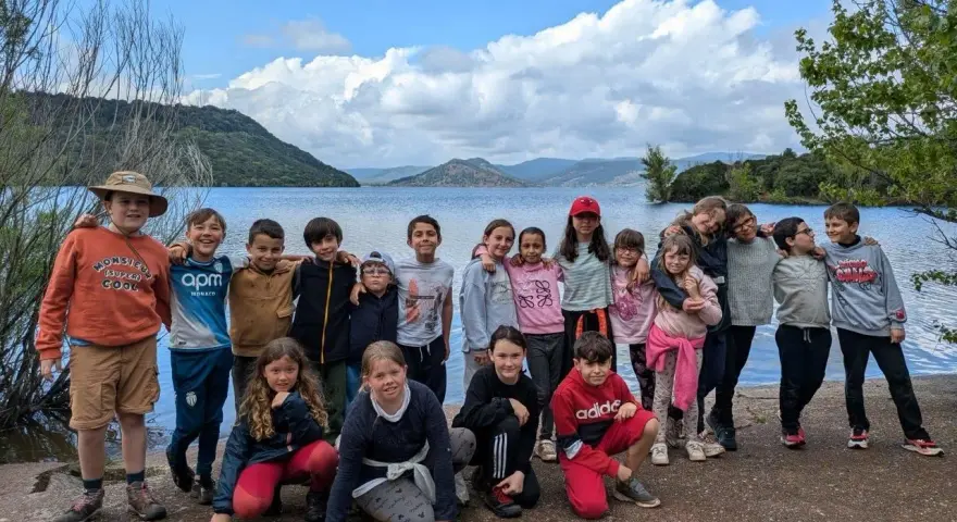 Un animateur pour combien de jeunes ? Un groupe d'enfants souriants pose devant un lac, prêts pour l'aventure.