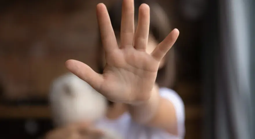Main d'enfant tendue, stop. Un doudou flou à côté. Une image qui évoque une cellule enfance en danger.