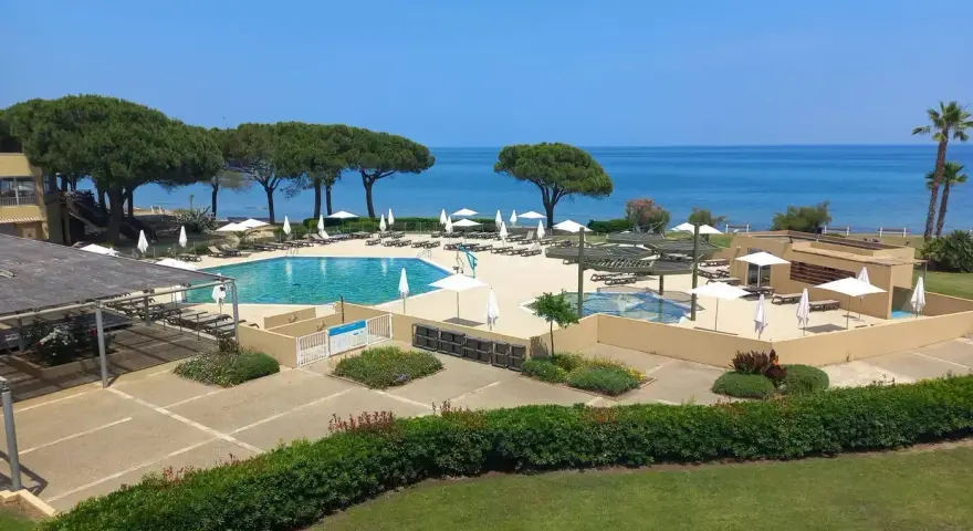 Piscine et transats dans un complexe hôtelier en bord de mer, sous un ciel bleu.